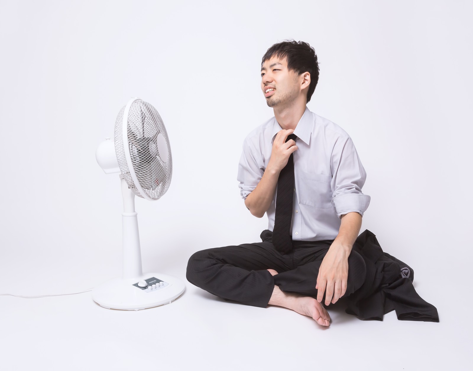 扇風機で涼もうとする男性の画像