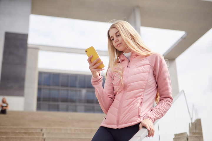 外出先でスマホにイヤホンをつけて音楽を聴く女性
