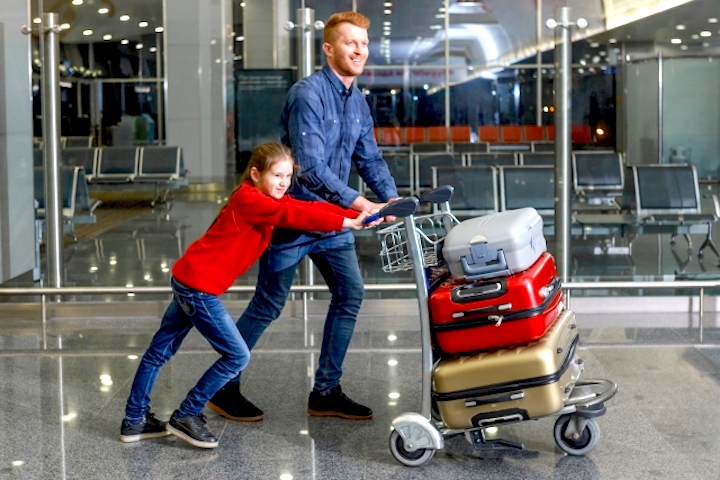 空港で親子がスーツケースを運ぶ写真
