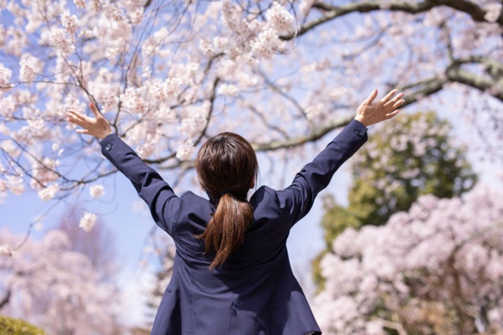 桜に向かって手を広げている新社会人