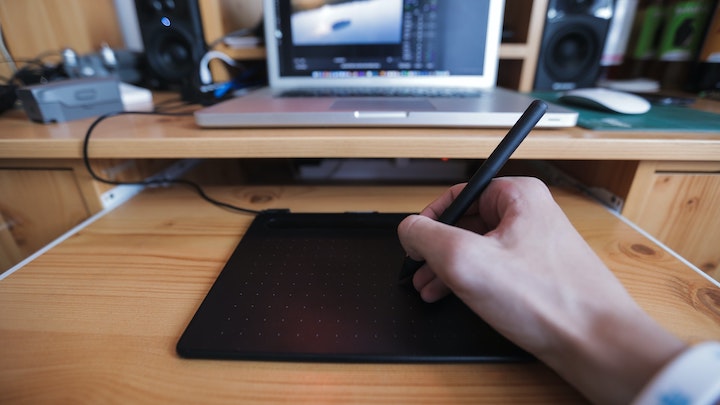 液晶タイプのペンタブで絵を描いている人の手の写真