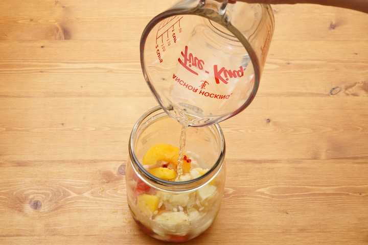 瓶に入れたスムージーの材料に水を注ぐ