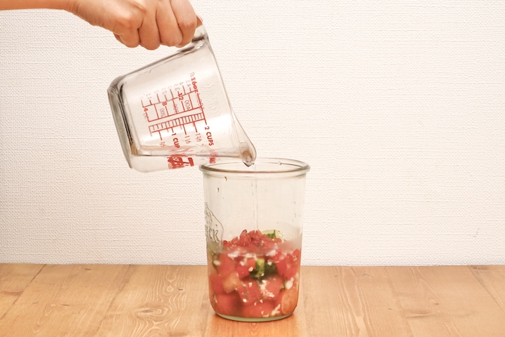 瓶に入れたスムージーの材料に水を注いているシーン