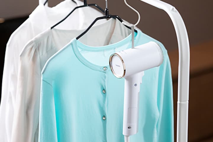 ハンガーにぶら下がっている洋服とハンディスチーマーの写真