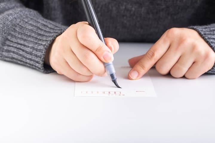 はがきに文字を書く女性の手
